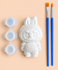 White bunny-eared plaster figure with three paint pots and two blue-handled brushes